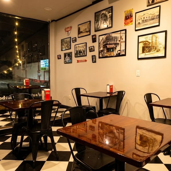 Cozy restaurant interior with checkered floor, dark wooden tables, black chairs, and framed pictures on the wall.